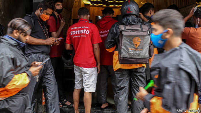 Delivery riders for Zomato Ltd., center, and Swiggy, operated by Bundl Technologies Pvt., wait to collect orders outside a restaurant in Mumbai, India, on Friday, July 16, 2021. Zomato $1.3 billion initial public offering was fully subscribed on the first day of sale, after anchor funds including BlackRock Inc. bid for 35 times more stock than was offered to them. Photographer: Dhiraj Singh/Bloomberg via Getty Images